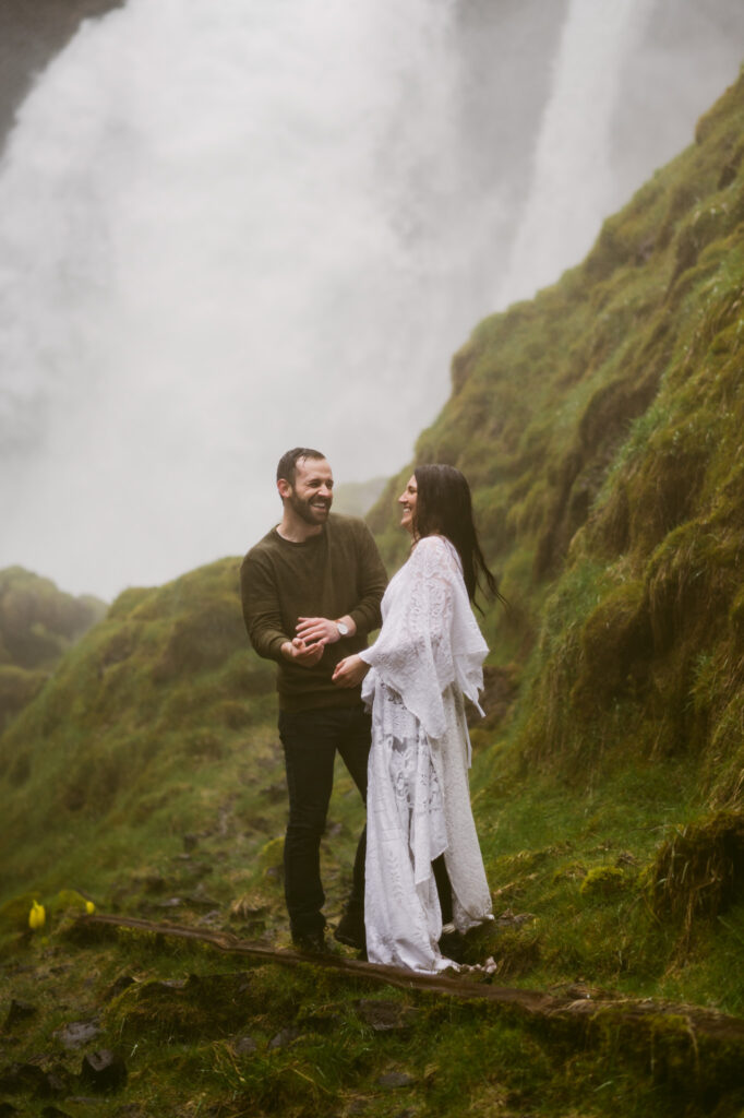 A bride and groom stand at the base of Sahalie Falls in Oregon. They are facing each other and laughing as they get soaked with the spray coming off of the falls.