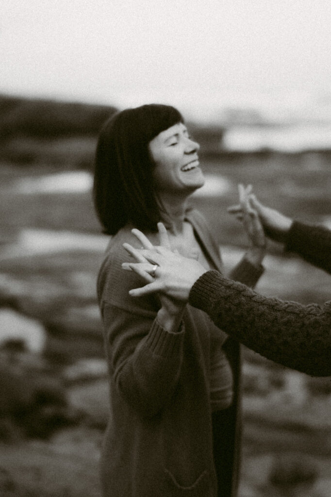 A black and white image of a woman laughing. She is slightly out of focus and standing on a beach.