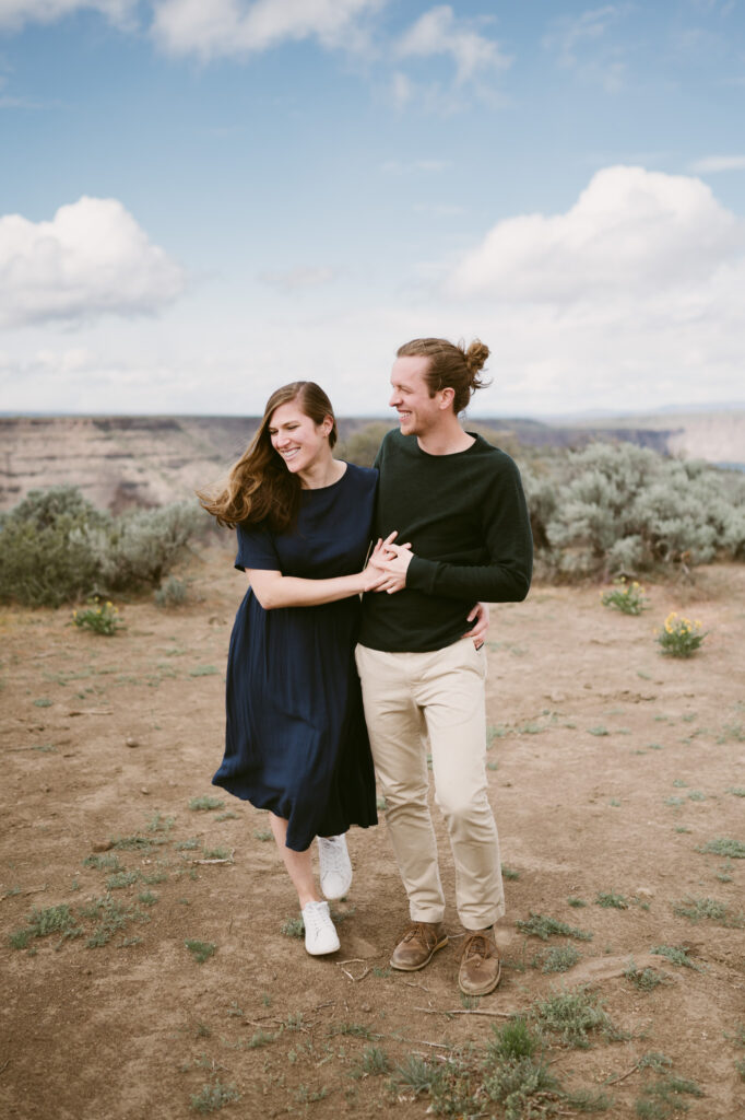 A man and woman walk towards the camera, embracing and laughing on the Tam-a-lau Trail at Cove Palisades.