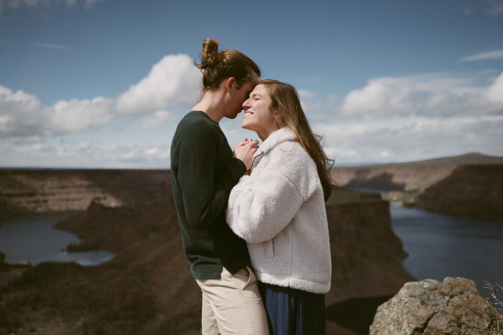 A man and woman stand in the bright sunlight, holding hands and leaning into each other. The woman's eyes are closed, face turned towards the sun.