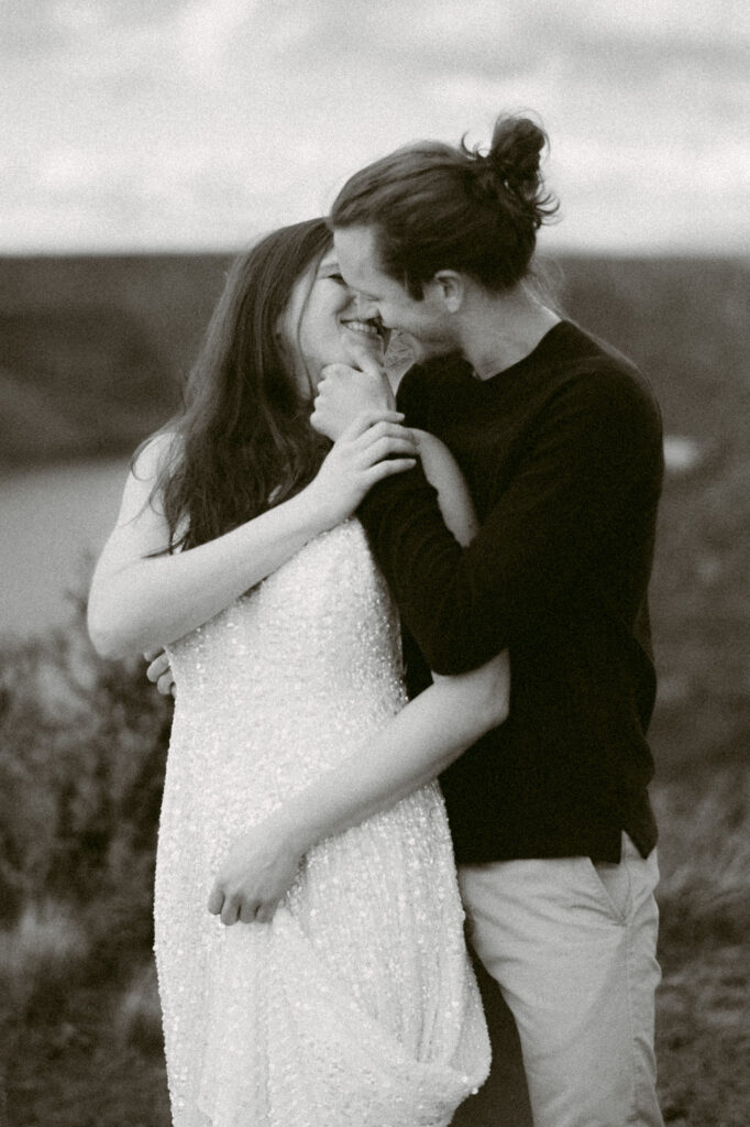 A black and white image of a man and woman at Cove Palisades State Park in Oreon. The woman's back is against the man's chest and he is gently kissing her.