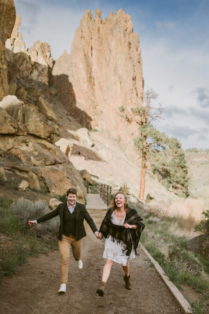 Two women hold hands and run towards the camera at Smith Rock State Park in central Oregon.