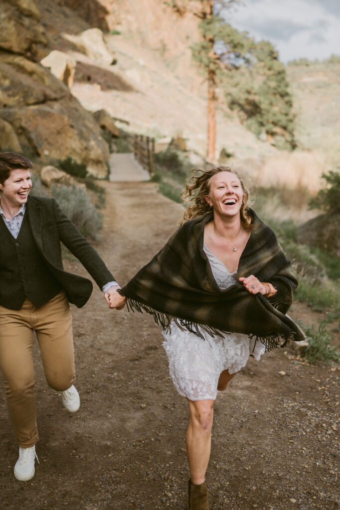 Two women hold hands and run towards the camera at Smith Rock State Park in central Oregon.