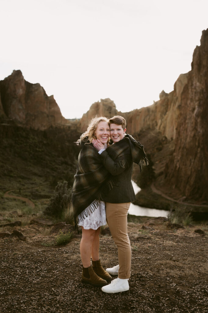 Two women stand in a tight embrace at an overlook at Smith Rock State Park. The rock formations frame their heads while the river disappears into the distance below.