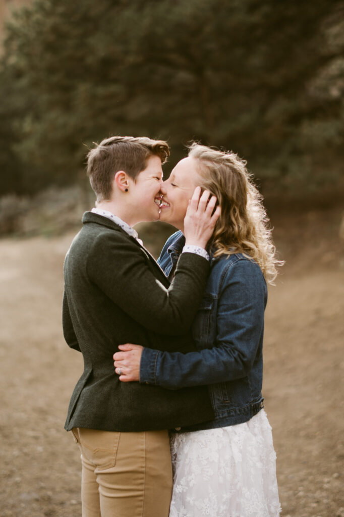 Two women lean in for a kiss. The first woman has her hand on the other's waist. The second woman is tucking the first woman's hair behind her ear as they kiss.