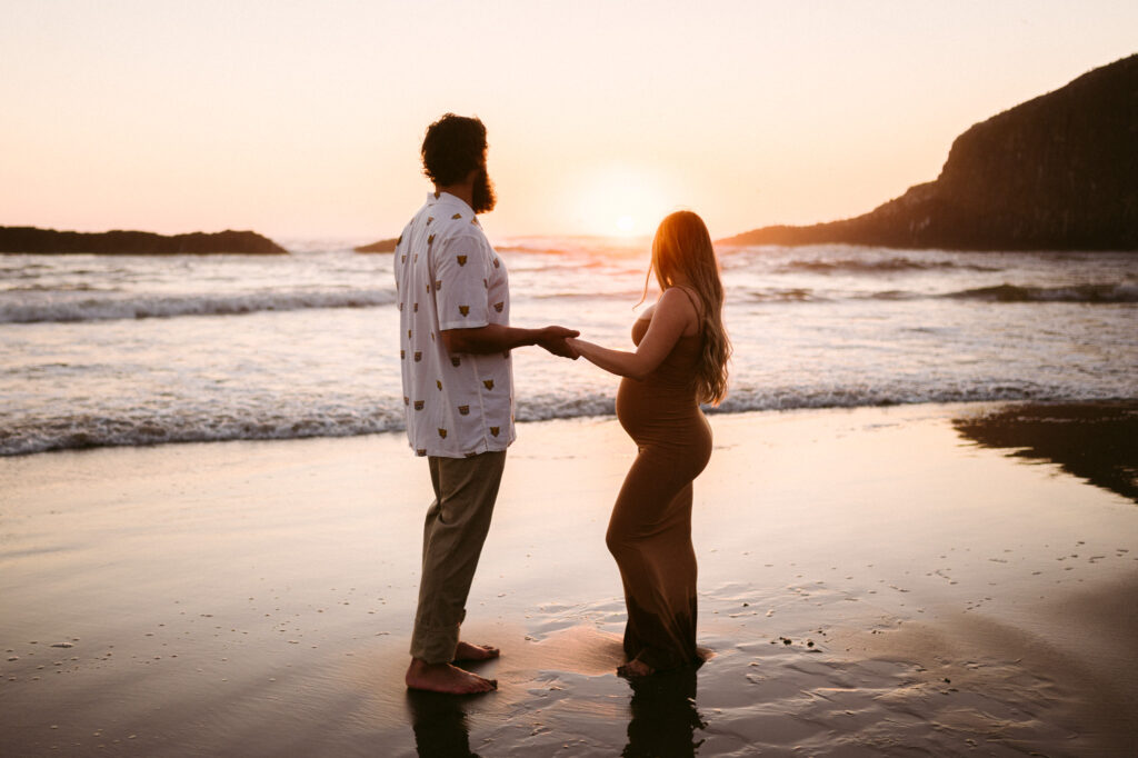 A husband and wife are silhouetted by the setting sun during their maternity session at Seal Rock Recreation Site in Seal Rock, Oregon.