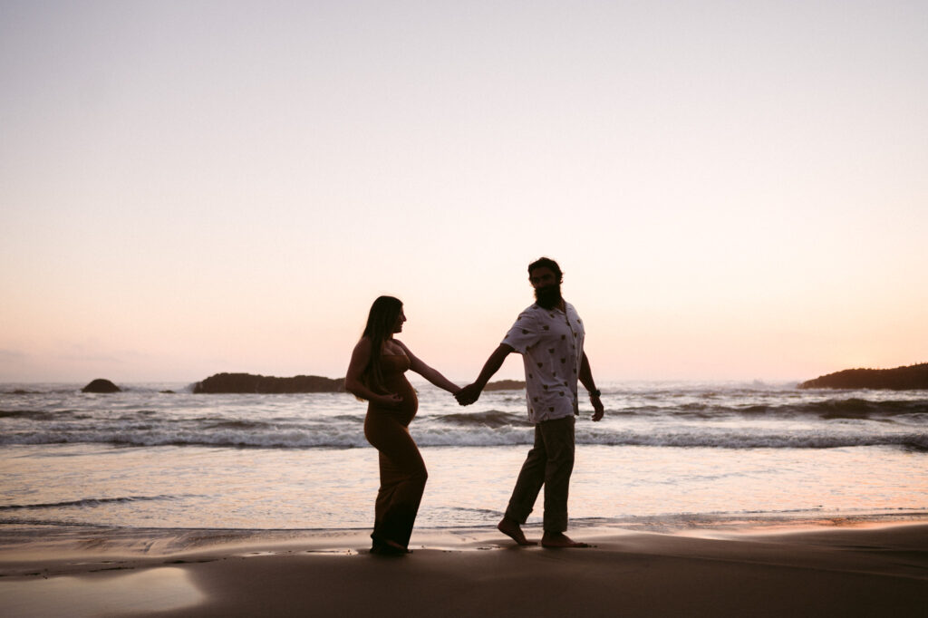 A husband and wife are silhouetted by the setting sun during their maternity session at Seal Rock Recreation Site in Seal Rock, Oregon.