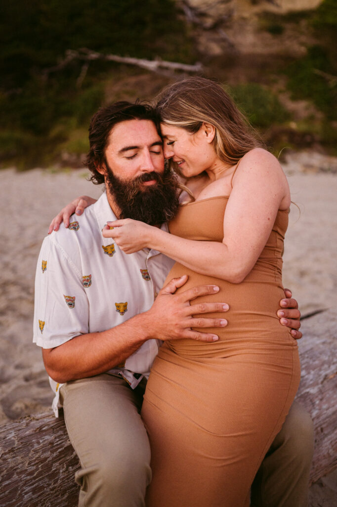 A young couple embraces on a log during their maternity session at Seal Rock Beach in Seal Rock, Oregon.