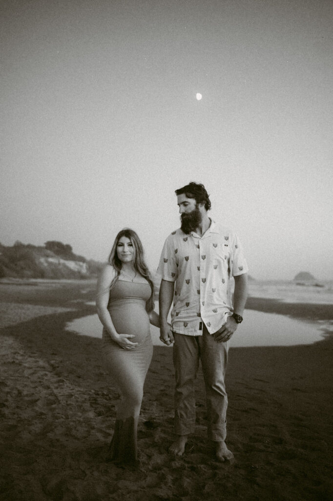 A black and white image of a young couple posing at twilight on Seal Rock Beach during their engagement session in Seal Rock, Oregon.