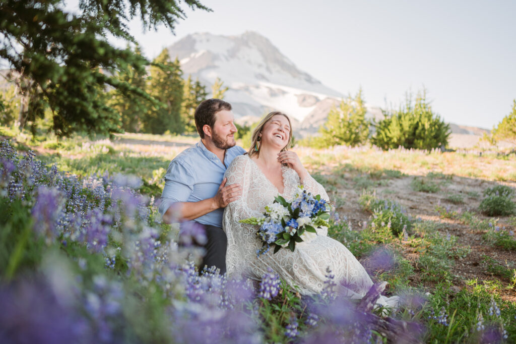 A bride and groom sit amongst a field of lupines during their elopement at Mount Hood Meadows. The summit of Mount Hood looms in the background.