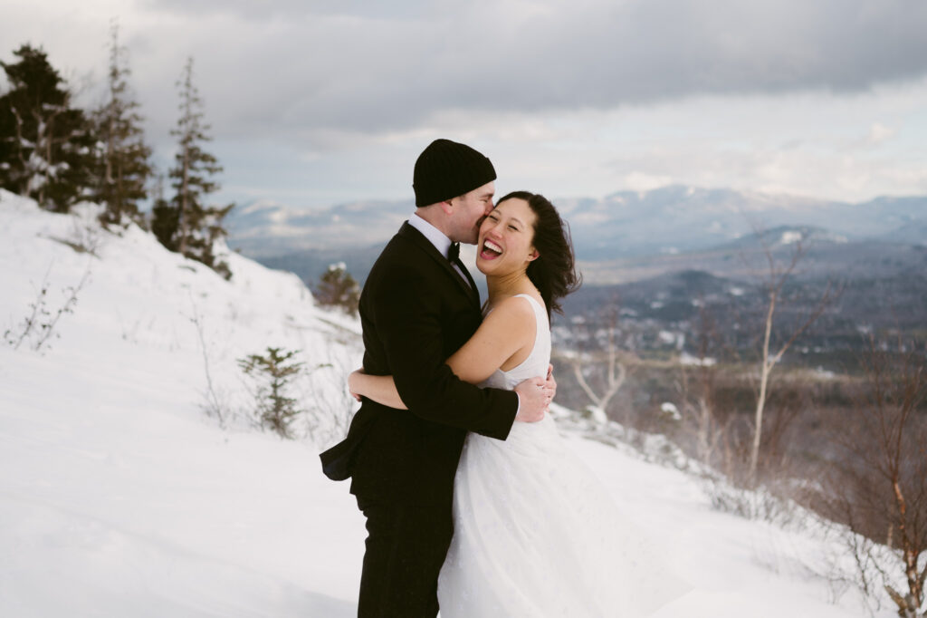 A recently married couple smile and kiss during their Adirondack elopement.