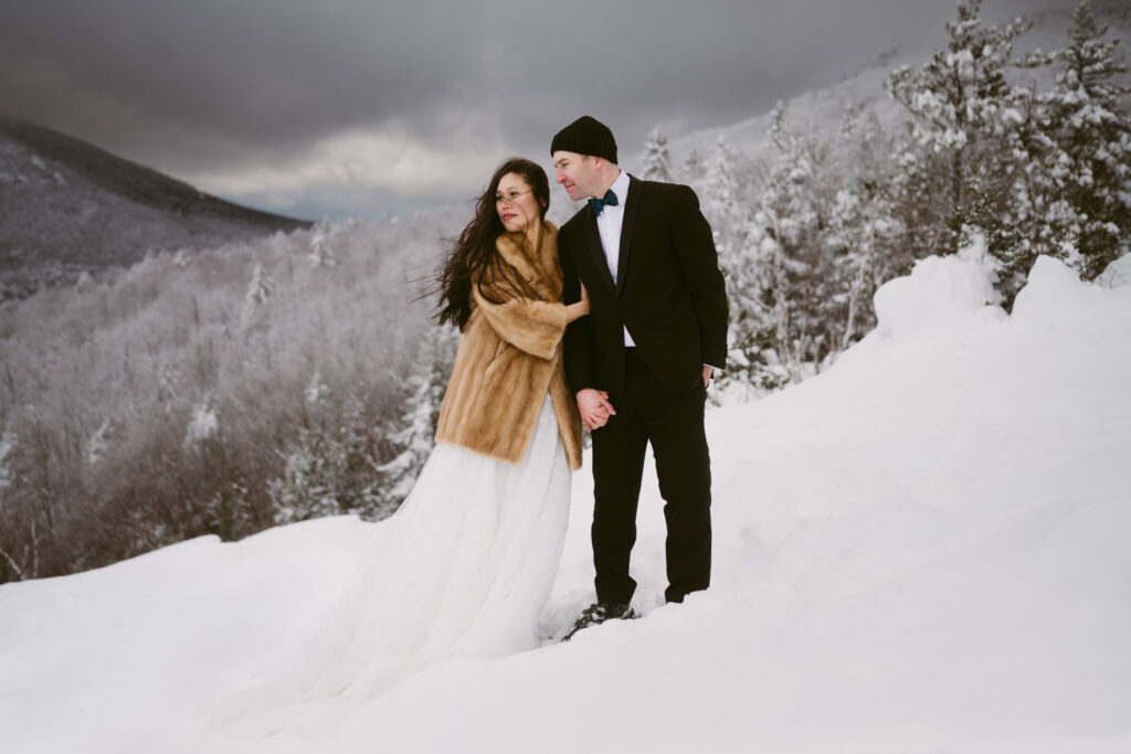 A bride and groom stand in a snowy mountain landscape during their winter Adirondack elopement in Lake Placid, NY.