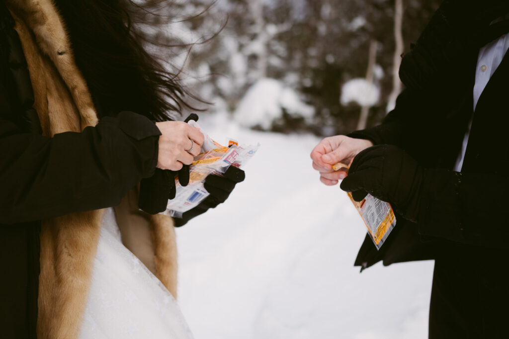 A bride and groom open hand warmers during their winter elopement in the Adirondack Mountains.