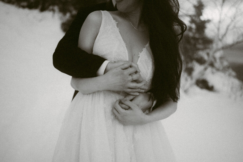 A close-up black and white image of two pairs of hands intertwined over a woman's chest and abdomen.