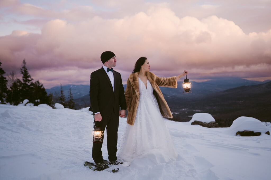 A bride and groom hold lanterns as the sun begins to set during their winter Adirondack elopement.