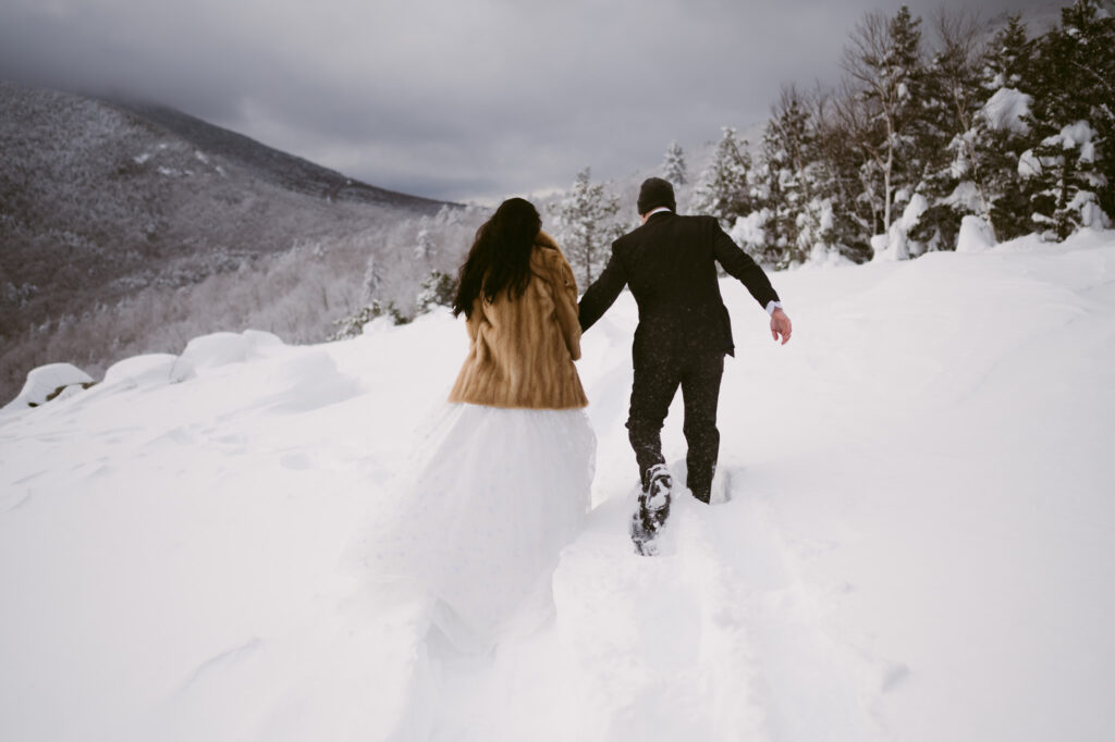 A bride and groom, bundled up and wearing snowshoes, wade through the deep snow during their winter elopement in Lake Placid, New York.