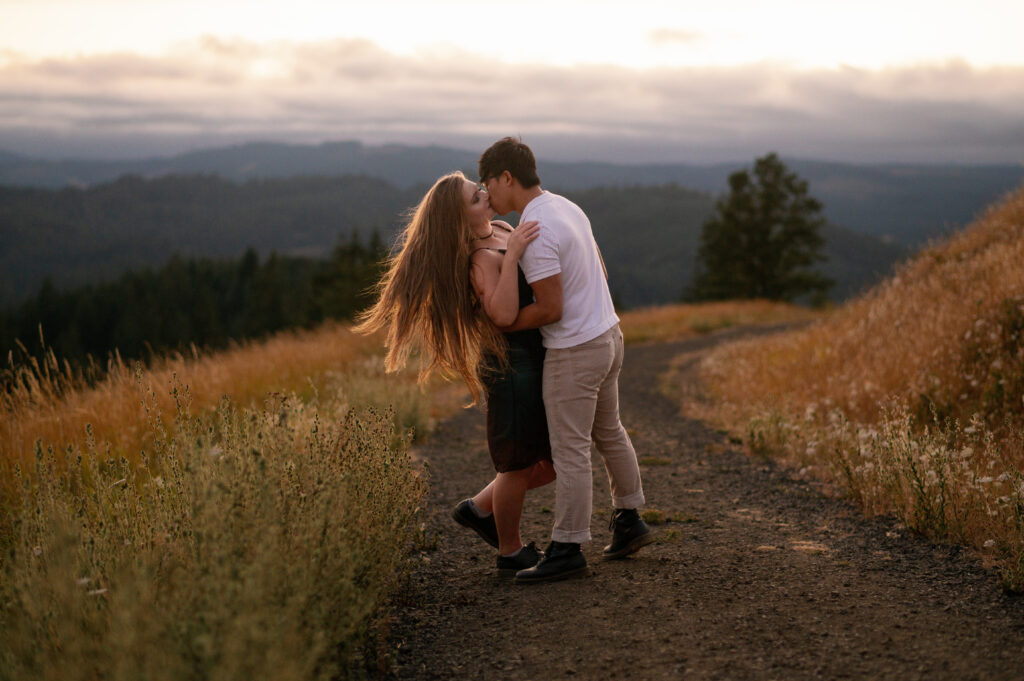 Couple embracing on a scenic dirt trail at sunset in Fitton Green Natural Area, surrounded by golden meadows and hills.