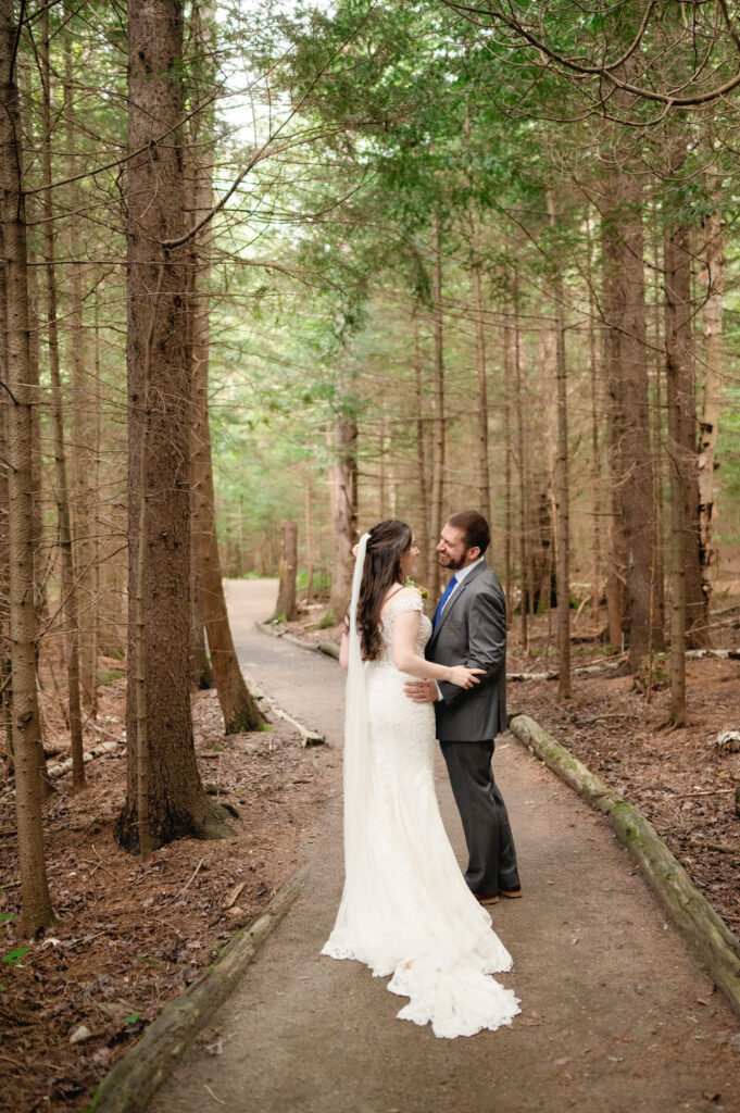 	The moment of the first look—Eric turns to see Martha for the first time on their wedding day, their eyes meeting with joy and quiet emotion. The forest trail provides a secluded, natural setting for their intimate moment.