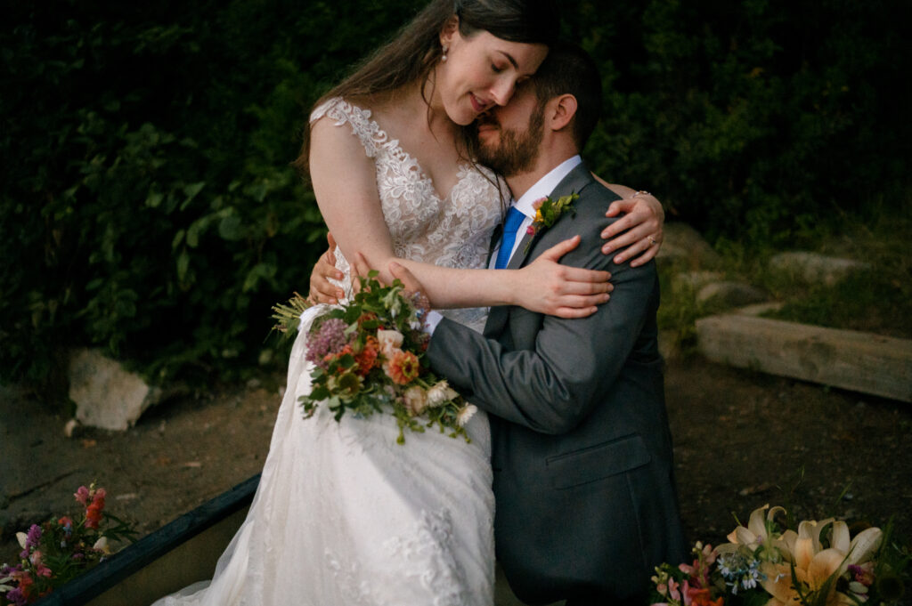 A close-up of the couple embracing in the canoe, with the bride resting her forehead against the groom’s as she cradles her bouquet.