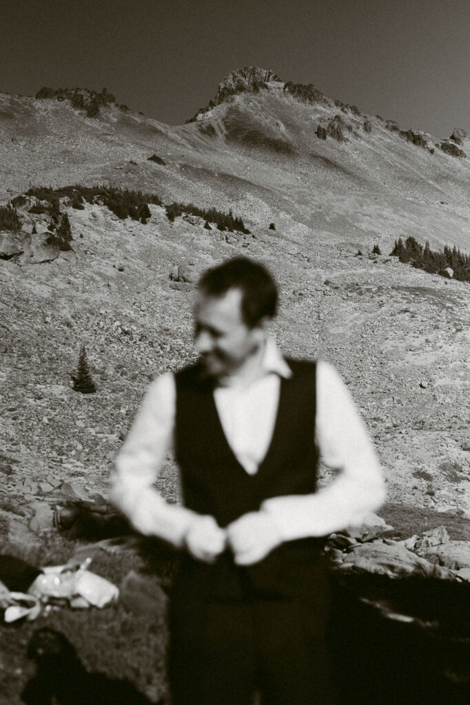 Candid black and white portrait of the groom adjusting his vest in front of Old Snowy Mountain before a hiking elopement in Goat Rocks Wilderness.