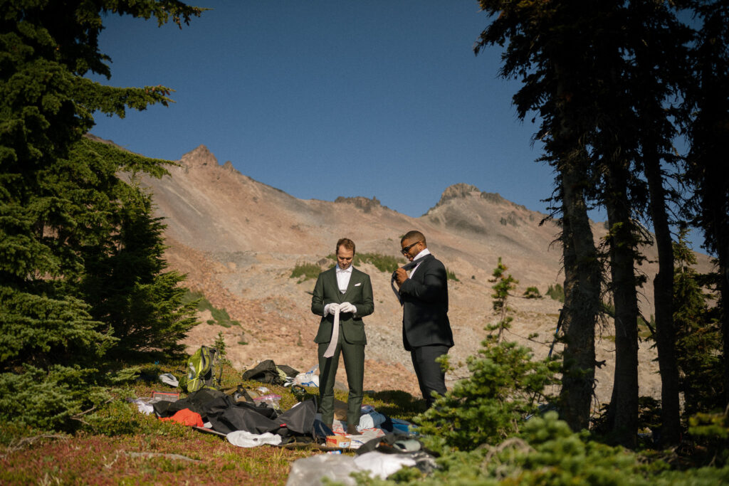 Groom and friend getting dressed in suits on the mountainside before an elopement ceremony in Goat Rocks Wilderness, Washington.
