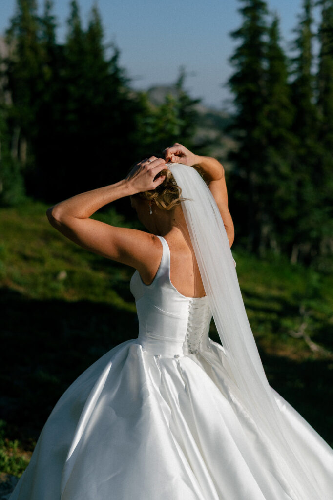 Bride securing her veil among alpine trees while getting ready for her Goat Rocks Wilderness elopement in Washington.