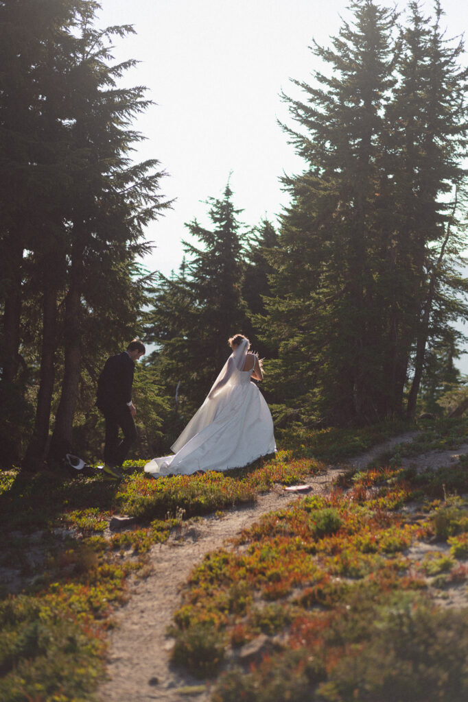 Bride in a flowing gown walking through the forest with her friend during her PCT hiking elopement in Goat Rocks Wilderness.
