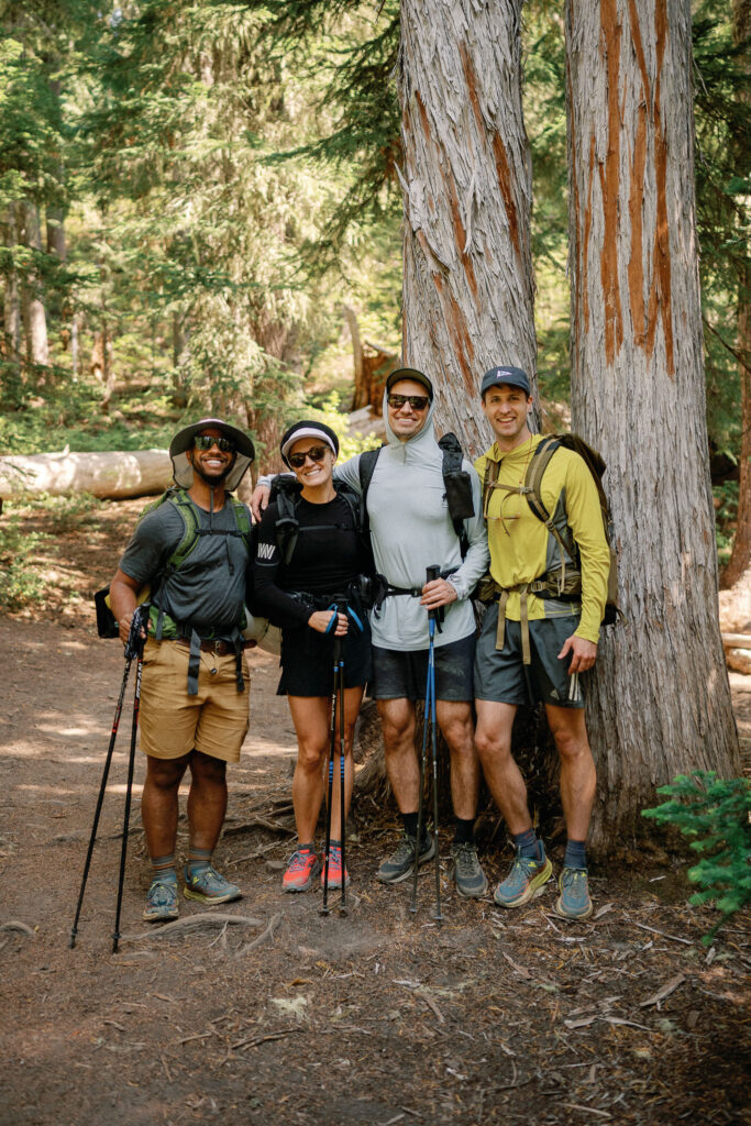 Elopement couple and close friends in hiking gear, smiling together among old-growth forest near Snowgrass Trailhead in Goat Rocks Wilderness.