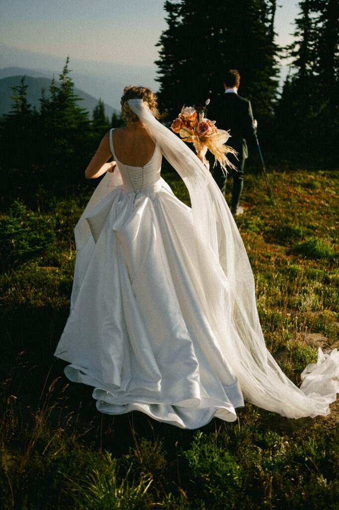 Bride carrying a bouquet and walking behind her groom on the Pacific Crest Trail during their wilderness elopement near Old Snowy Mountain.