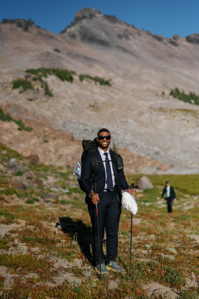 Groomsman dressed in a suit with a backpack and trekking poles during a backcountry hiking elopement in Goat Rocks Wilderness, WA.