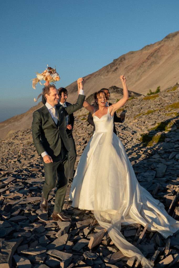 The newlyweds raise their joined hands triumphantly after the ceremony, bouquet held high and faces full of joy.