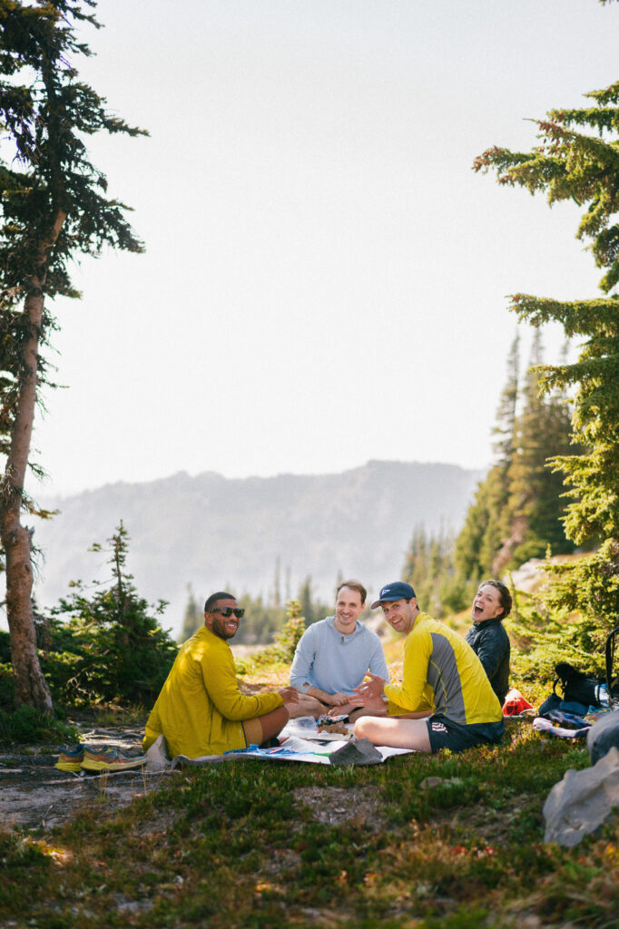 Wedding couple and friends laughing together at a backcountry picnic spot during their PCT elopement in Goat Rocks Wilderness, Washington.