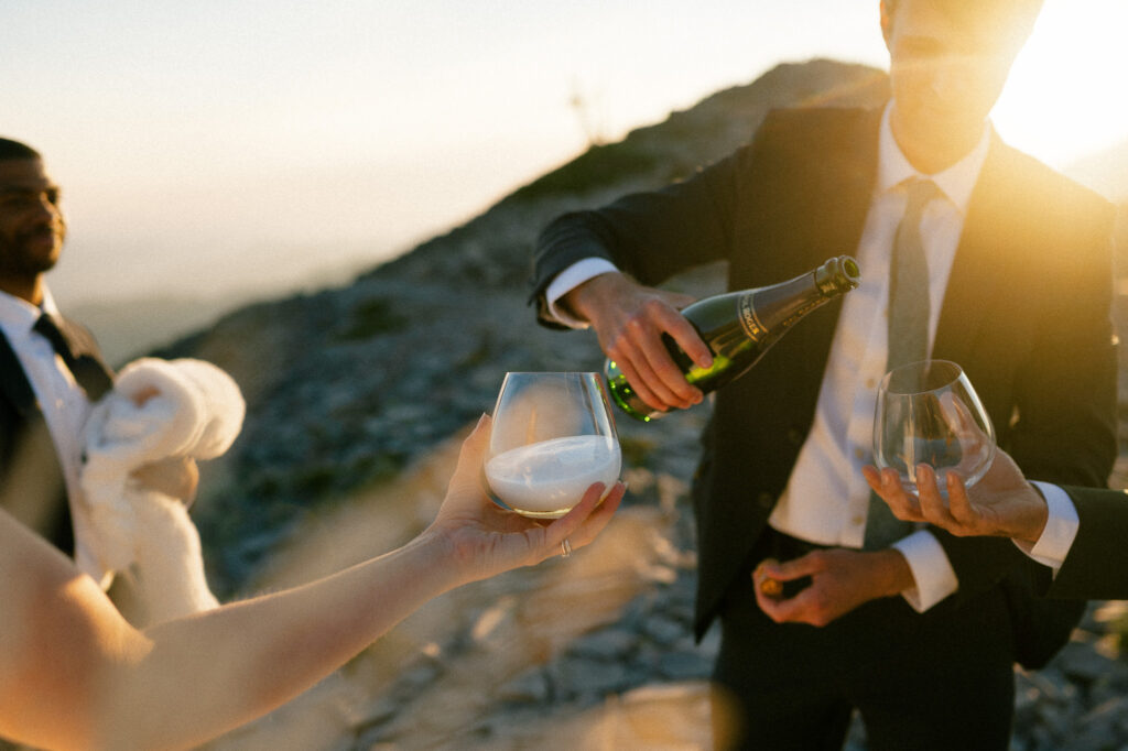A celebratory moment as champagne is poured into glasses held by the couple and their guests atop a mountain.