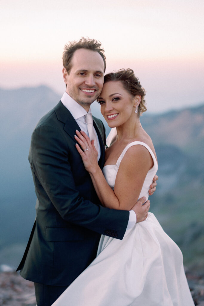Portrait of the couple standing close together, smiling and embracing as the soft light of twilight falls behind them.