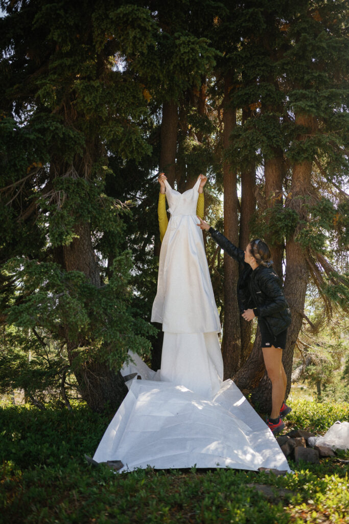 Bride and friend hanging wedding dress in the forest during a hiking elopement prep moment in Goat Rocks Wilderness, along the PCT.