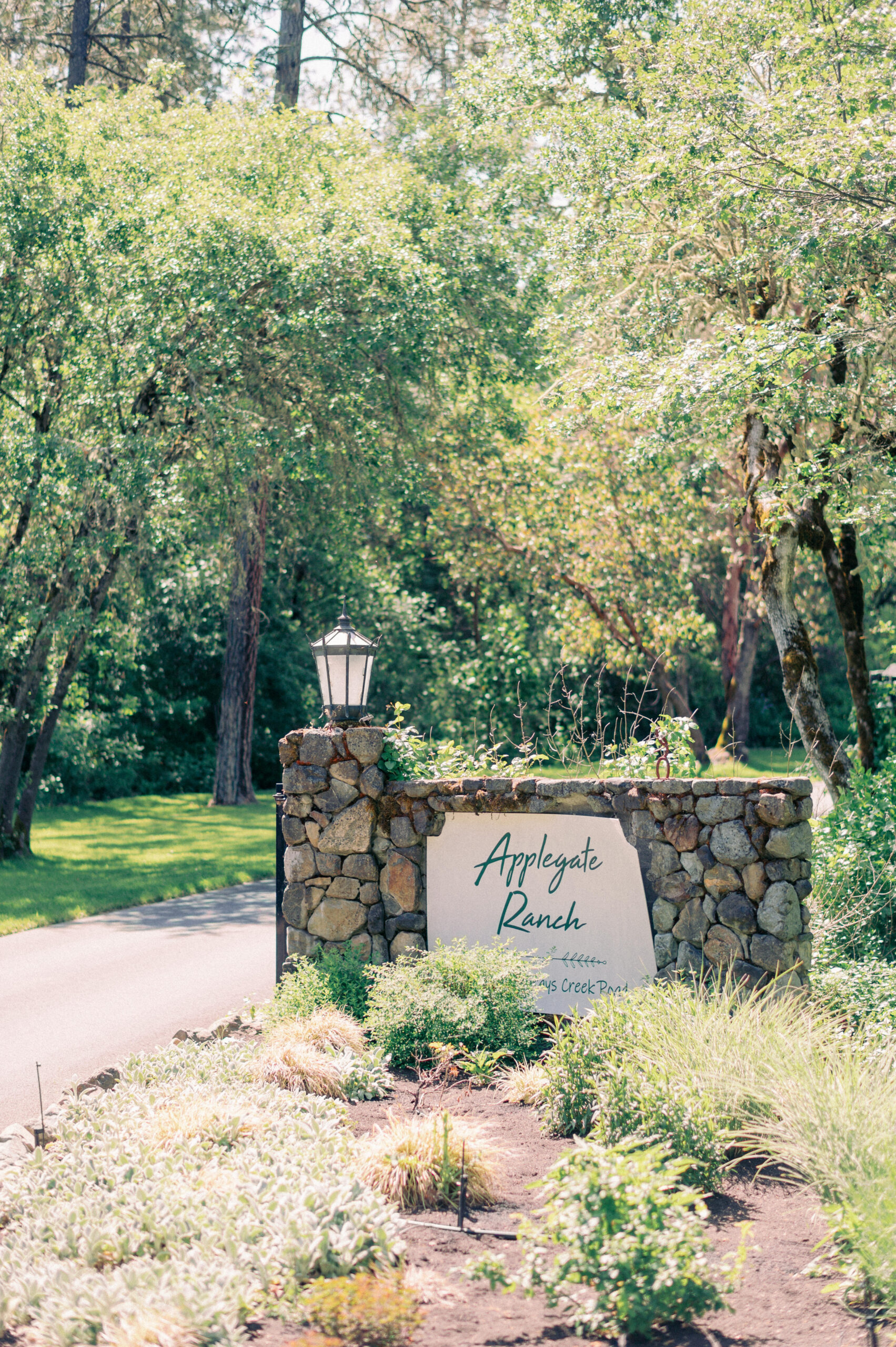 Stone entry sign at Applegate Ranch wedding venue in Grants Pass, Oregon, surrounded by lush greenery and trees in late spring.