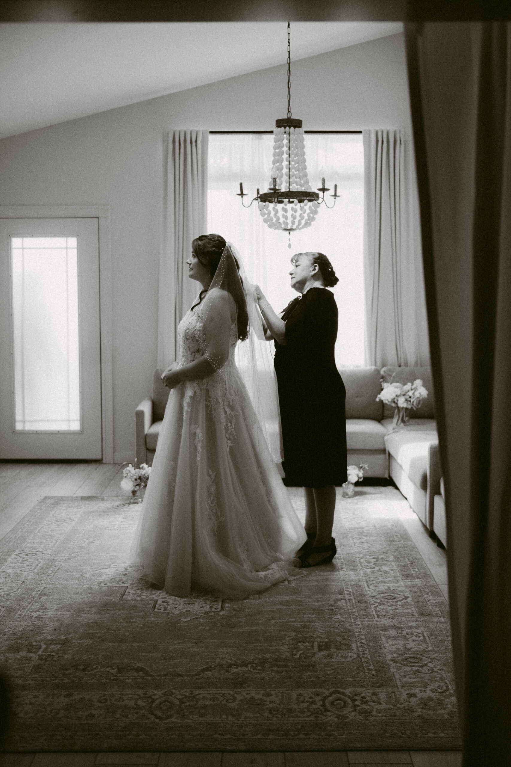 Emotional black-and-white photo of the bride’s mother gently adjusting her veil in a softly lit room before the ceremony.