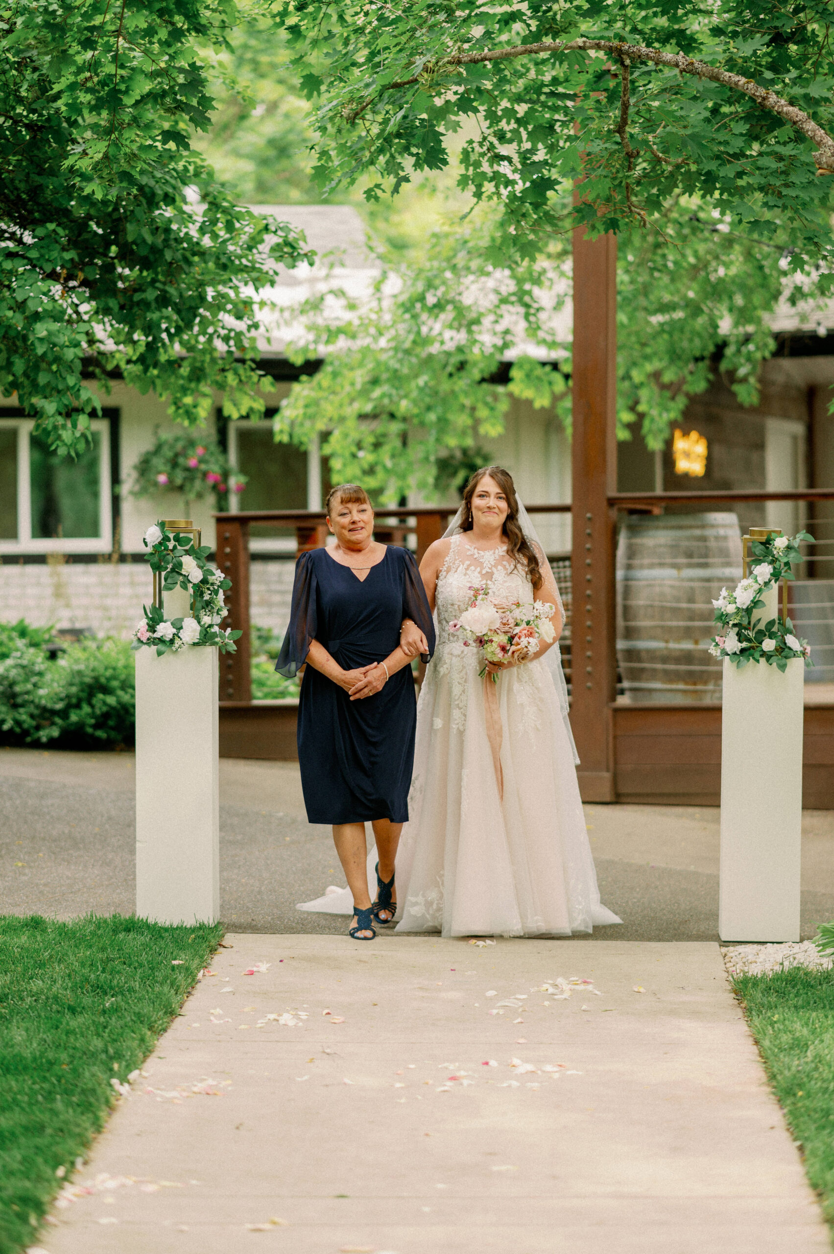 Bailey walks down the aisle arm in arm with her mother, both smiling as they approach the ceremony arch.