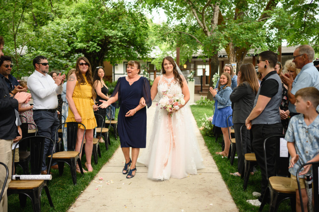 Bailey walks down the aisle arm in arm with her mother, both smiling as they approach the ceremony arch.