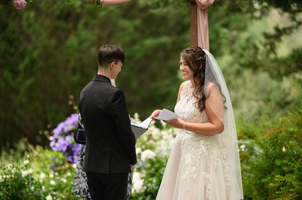 Bride and bride exchanging vows under a floral-draped arch during their outdoor ceremony at Applegate Ranch.