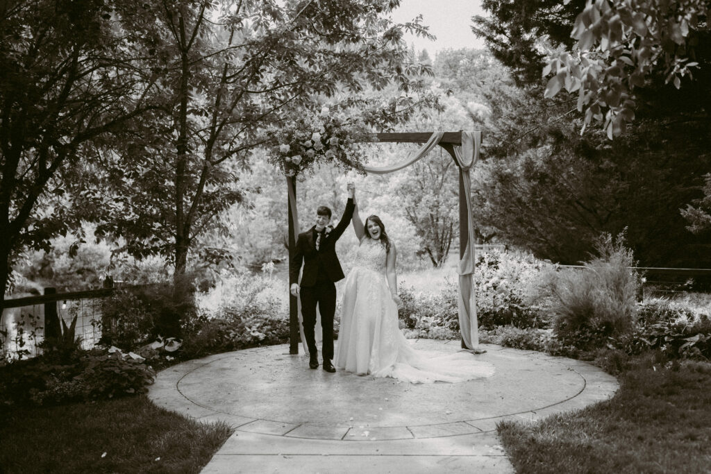 Just married moment as the couple raises their joined hands triumphantly under the ceremony arch.