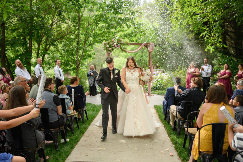Recessional moment as the couple walks hand in hand down the aisle while guests cheer and pop confetti cannons.