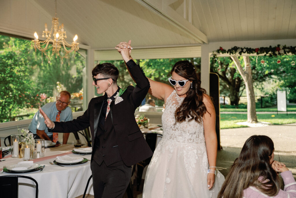 Newlyweds enter reception wearing heart-shaped sunglasses and holding hands in celebration.