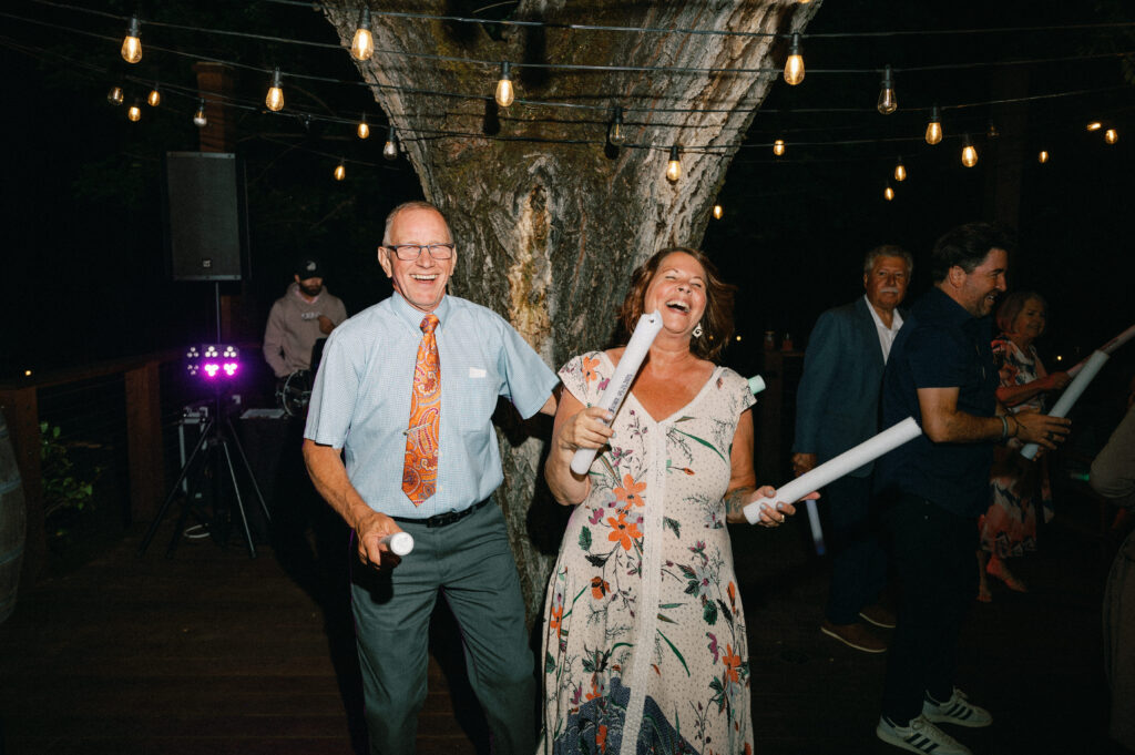 Guests dancing under bistro lights on the wooden deck at Applegate Ranch, joyfully waving foam glow sticks.
