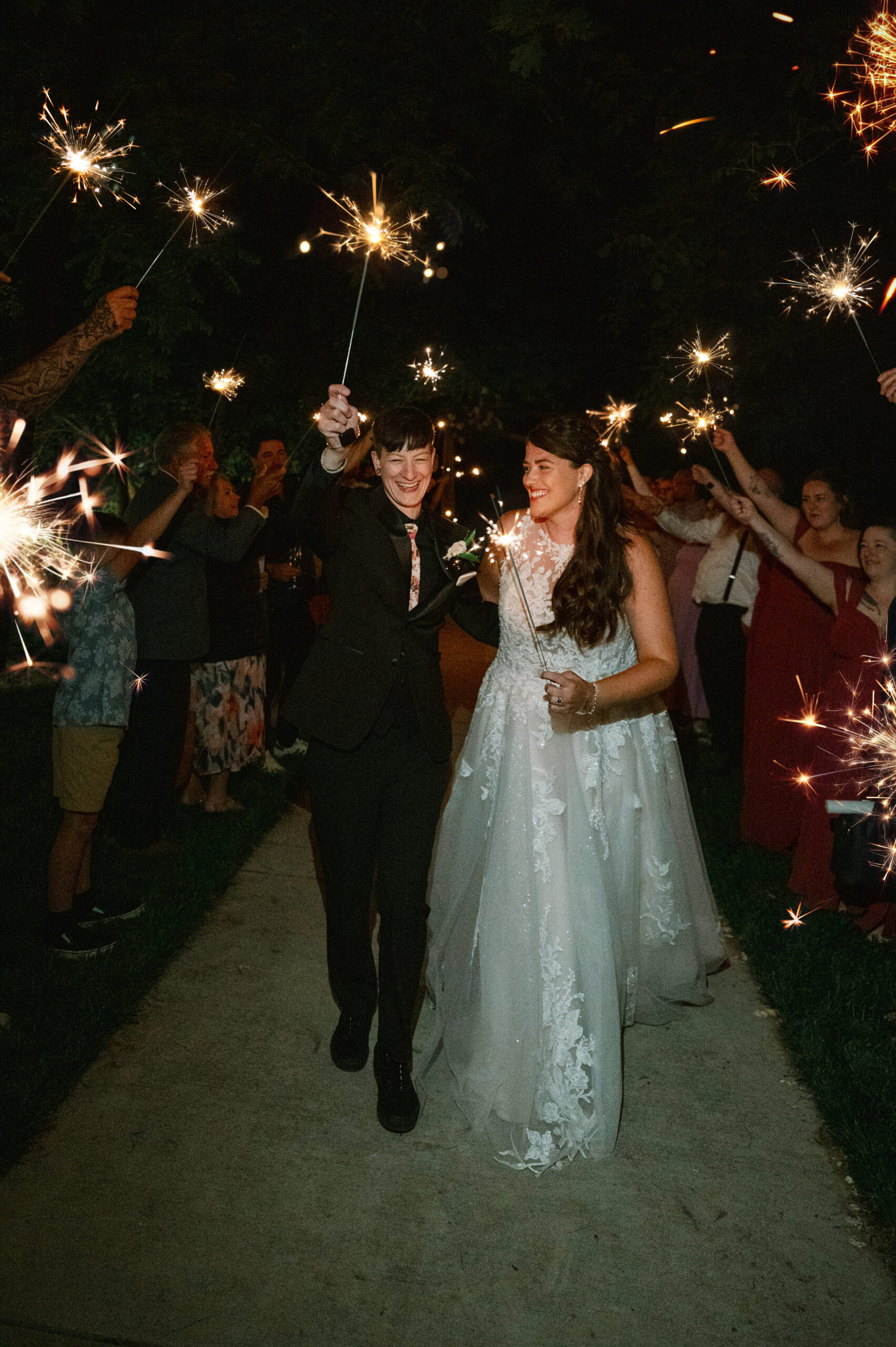 A joyful sparkler exit as guests line the path, cheering while the brides walk hand in hand through the glowing tunnel.