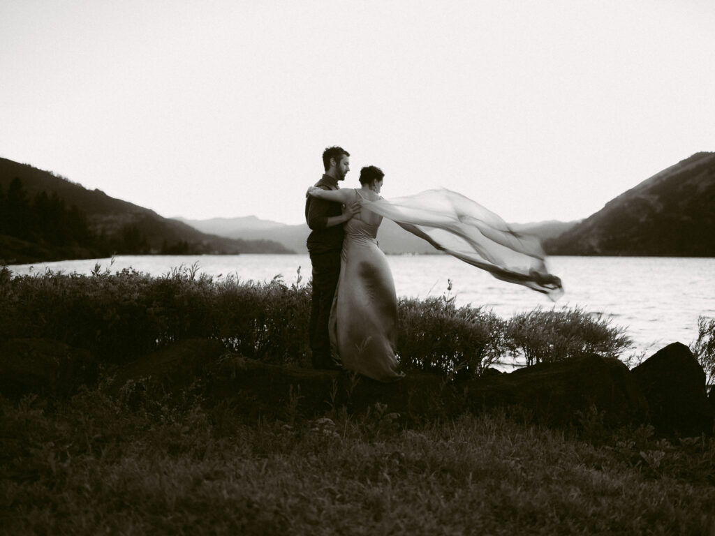 The bride gazes over her shoulder toward the Columbia River at sunset, her veil softly catching the breeze.