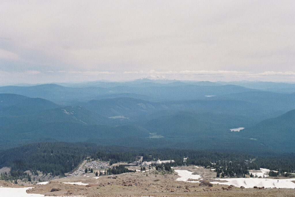 A soft 35mm film photograph capturing the sweeping Cascade Range from high on Mount Hood, with Timberline Lodge far below.