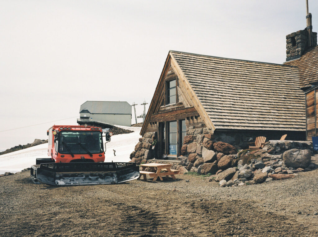 A bright red Snowcat parked beside the stone exterior of Silcox Hut, ready to transport guests up Mount Hood.