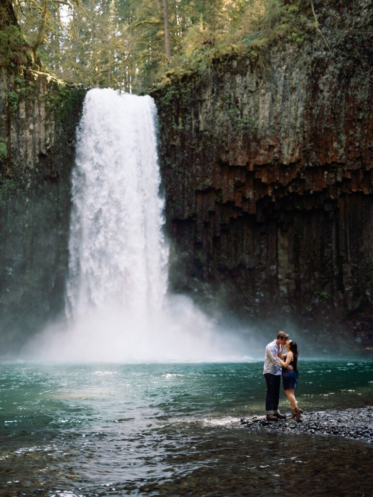 An engaged couple pauses to kiss in front of Abiqua Falls during their engagement session.