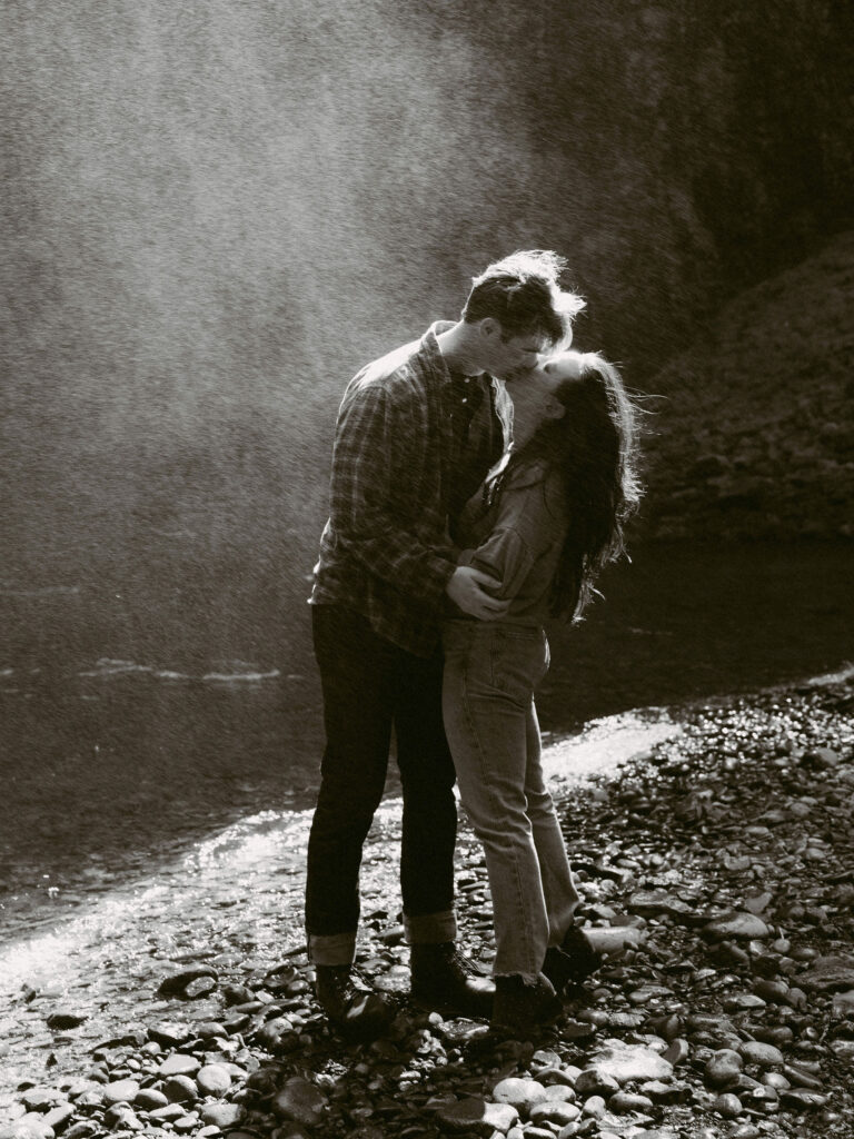An engaged couple kisses in the windy mist of Abiqua Falls during their engagement photos.